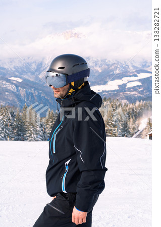 Male skier standing on snowy mountain slope with alpine landscape Male skier standing on snowy mountain slope with alpine landscape 138282721
