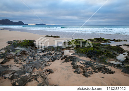 A picturesque beach with algae-covered rocks, waves meeting the shore A picturesque beach with algae-covered rocks, waves meeting the shore 138282912