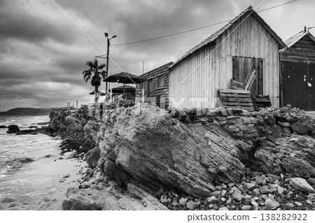 Weathered wooden boat barns sit along a rocky shoreline under a cloudy sky 138282922