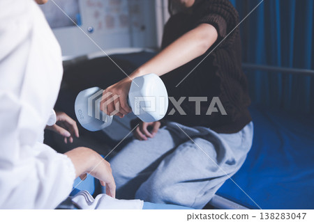 Old woman training with physiotherapist using dumbbells at home. Therapist assisting senior woman with exercises in nursing home. Elderly patient using dumbbells with outstretched arms. 138283047