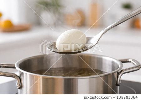 Boiled egg on spoon above pot with steam in kitchen cooking process Boiled egg on spoon above pot with steam in kitchen cooking process 138283364
