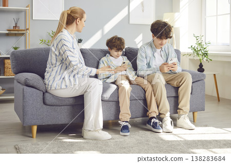 Young mother arguing with her children sitting on sofa addicted from mobile phone. 138283684