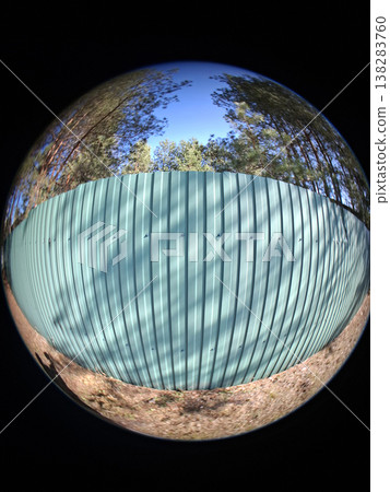 A green corrugated metal fence stands tall in front of a background of pine trees under a clear blue sky. This scene highlights themes of security and property protection. A green corrugated metal fence stands tall in front of a background of pine trees under a clear blue sky. This scene highlights themes of security and property protection. 138283760