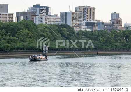 黃昏時分,一艘船屋沿著大川緩緩駛過,大阪的城市景觀在遠處映入眼簾。 黃昏時分,一艘船屋沿著大川緩緩駛過,大阪的城市景觀在遠處映入眼簾。 138284340