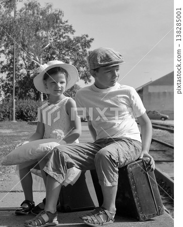 Children in vintage clothing waiting with luggage at a train station Children in vintage clothing waiting with luggage at a train station 138285001