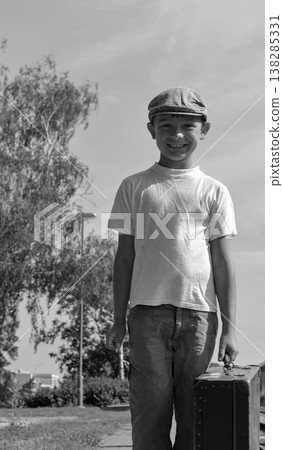 Smiling young boy in flat cap holding vintage suitcase ready for travel Smiling young boy in flat cap holding vintage suitcase ready for travel 138285331