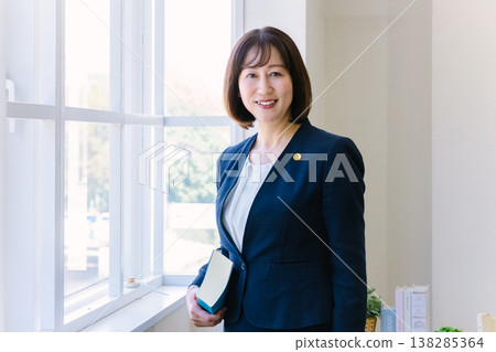 A female lawyer stands by the window at a law firm. A female lawyer stands by the window at a law firm. 138285364