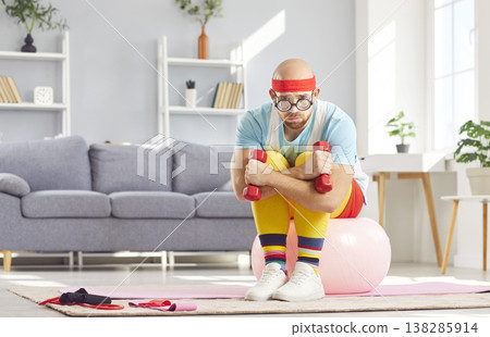 Eccentric man in funny sports outfit sitting with worried expression before sports training at home. Eccentric man in funny sports outfit sitting with worried expression before sports training at home. 138285914