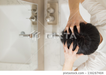 一位年輕男子在浴室裡梳頭。 138287484