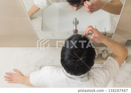 A young man doing hair care in the bathroom. 138287487