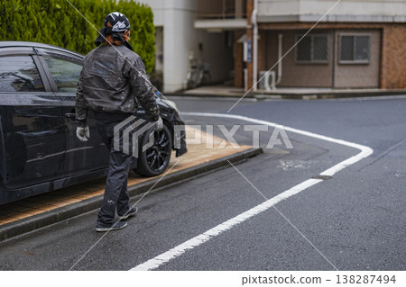 A man in work clothes is seen from behind, walking through a residential area; his face is not visible. A man in work clothes is seen from behind, walking through a residential area; his face is not visible. 138287494