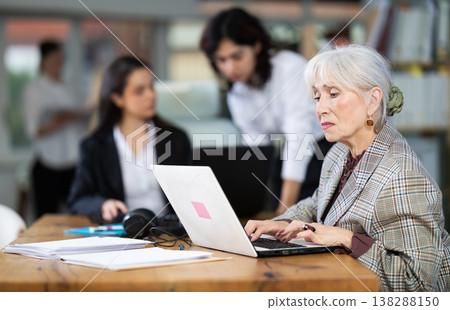 Elderly woman works on laptop with female colleagues Elderly woman works on laptop with female colleagues 138288150