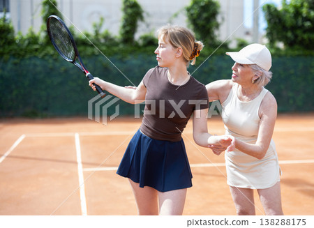 Senior female coach gives tennis lesson, teaches girl game Senior female coach gives tennis lesson, teaches girl game 138288175