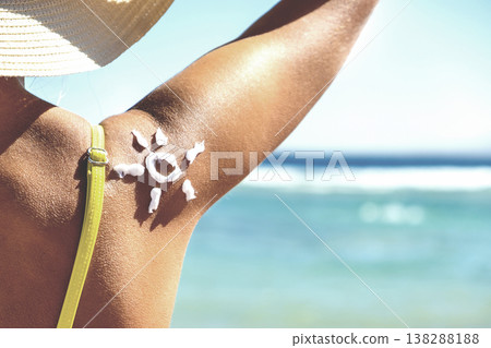 Back view of young woman tanning at the beach with sunscreen cream in sun shape on her shoulder. UV sunburn protection and sunblock skincare concept 138288188