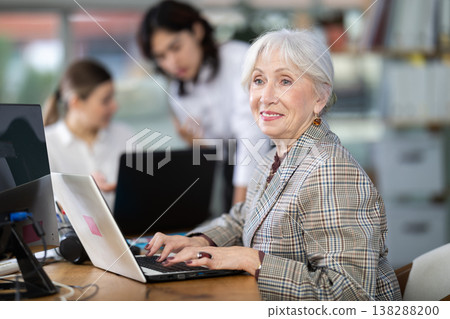 In office, senior woman is working on laptop as part of group of colleagues. In office, senior woman is working on laptop as part of group of colleagues. 138288200