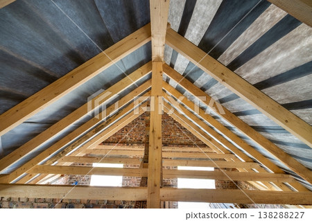 Attic of a building under construction with wooden beams of a roof structure and brick walls. Attic of a building under construction with wooden beams of a roof structure and brick walls. 138288227