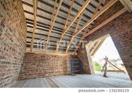 Attic of a building under construction with wooden beams of a roof structure and brick walls. Attic of a building under construction with wooden beams of a roof structure and brick walls. 138288229