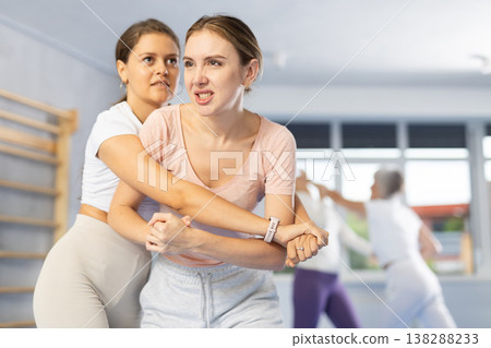 Woman trying to break free of rear grab, striking solar plexus with elbow during self-defense course 138288233