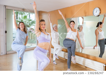 Class of women of different ages in sportswear training with knee up while learning dance moves with trainer in gym Class of women of different ages in sportswear training with knee up while learning dance moves with trainer in gym 138288247