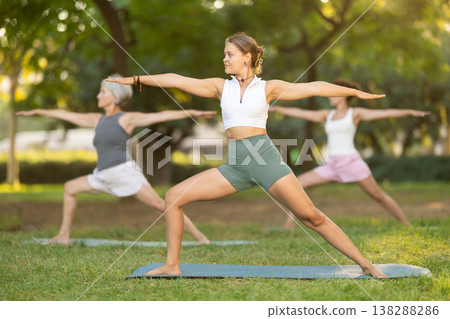 Happy woman standing yoga pose and making full body stretching workout with group people at park outdoor Happy woman standing yoga pose and making full body stretching workout with group people at park outdoor 138288286