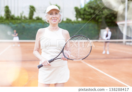 Senior woman in sportswear against backdrop of outdoor tennis court. 138288417