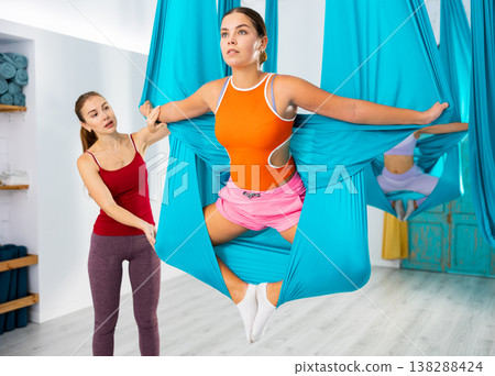 Woman aerial yoga instructor helping girl to perform butterfly pose in hammock Woman aerial yoga instructor helping girl to perform butterfly pose in hammock 138288424