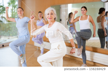 Cheerful senior female choreographer showing new dancing dynamic movements during training together with women in studio 138288429