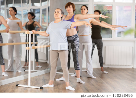 Women of different ages exercise near the ballet barre at group training session in batman batyu position Women of different ages exercise near the ballet barre at group training session in batman batyu position 138288496