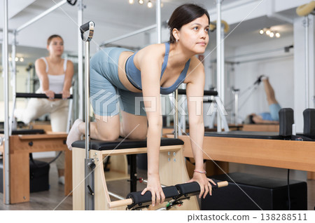 Focused woman performing set of pilates exercises on reformer in fitness studio. Healthy active lifestyle concept 138288511