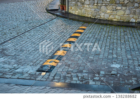 Industrial speed breaker on a wet stone pavement in an urban environment with stone walls Industrial speed breaker on a wet stone pavement in an urban environment with stone walls 138288682