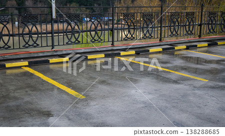 Empty parking lot after rain featuring yellow markings, a black fence, and a river background 138288685