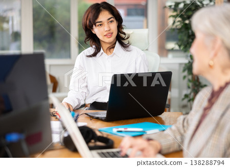 Positive young woman sitting at desk and typing on laptop in office 138288794