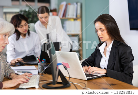 In office, young woman is working on laptop as part of group of colleagues. In office, young woman is working on laptop as part of group of colleagues. 138288833
