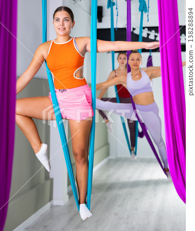 Young girl practicing group aerial yoga with hanging hammock Young girl practicing group aerial yoga with hanging hammock 138288894