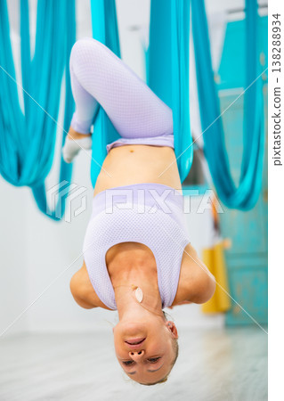 Woman doing inverted stag pose on hanging hammock in aerial yoga studio 138288934