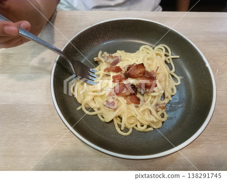 Spaghetti carbonara bacon cream sauce pasta fork hand wood table dinner lunch creamy spaghetti carbonara with crispy bacon deep plate wood table, hand holding fork twirling pasta for tasty meal Spaghetti carbonara bacon cream sauce pasta fork hand wood table dinner lunch creamy spaghetti carbonara with crispy bacon deep plate wood table, hand holding fork twirling pasta for tasty meal 138291745