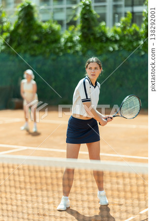 Young woman playing doubles tennis on court 138292001
