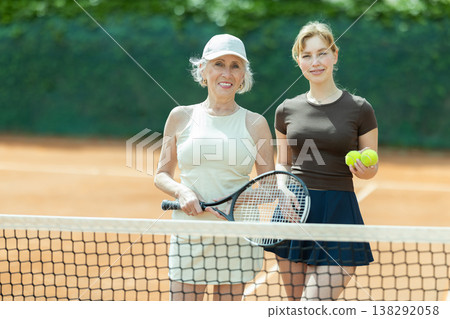 Girl and senior woman in sportswear against backdrop of outdoor tennis court. Girl and senior woman in sportswear against backdrop of outdoor tennis court. 138292058