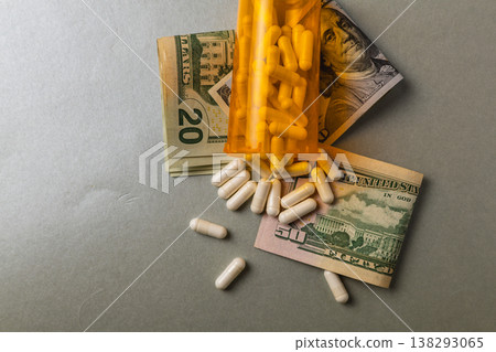 Pills spilled from bottle next to rolled up cash on gray surface Pills spilled from bottle next to rolled up cash on gray surface 138293065
