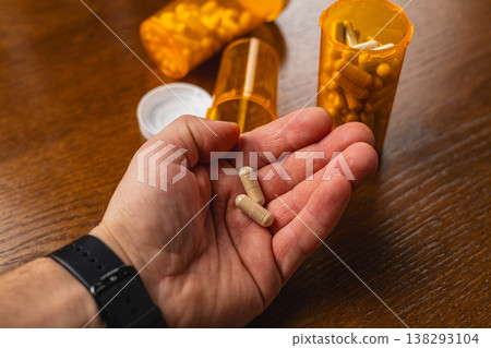 Hand holding capsules with prescription bottles on table during daytime Hand holding capsules with prescription bottles on table during daytime 138293104