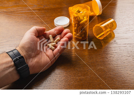 Hand holds capsules near orange prescription bottles on wooden table 138293107