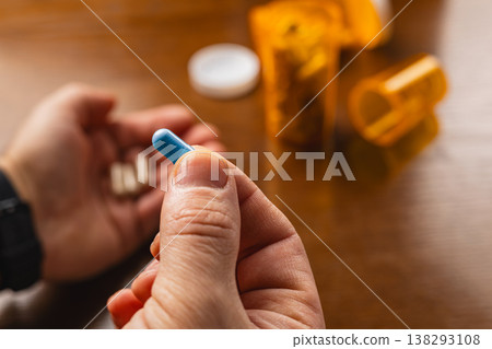 Holding a blue capsule while sitting near medicine containers on a table Holding a blue capsule while sitting near medicine containers on a table 138293108
