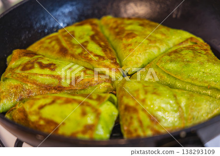 Green flatbreads cooking in a skillet on a stovetop in a kitchen 138293109