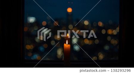 Burning candle on a windowsill overlooking a blurred night city skyline with warm bokeh lights and dark atmosphere. 138293296