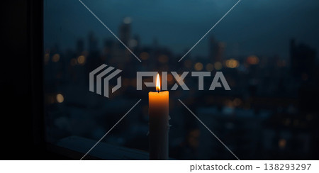 Lit candle on a wooden ledge overlooking a moody blue hour city landscape with blurred buildings and distant urban glow. 138293297