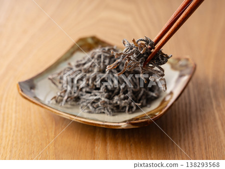 I lift the salted kelp from the wooden table and Japanese plate with my chopsticks. I lift the salted kelp from the wooden table and Japanese plate with my chopsticks. 138293568