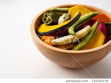 A wooden bowl and colorful vegetable chips placed against a white background. (Angled view. Copy space on the left.) 138293576