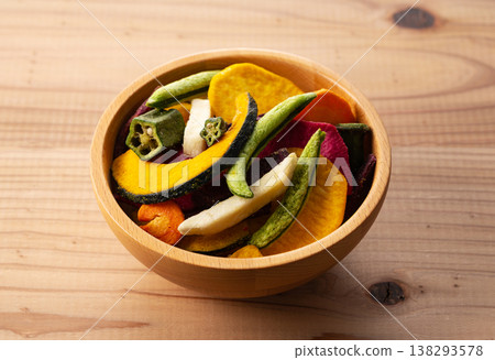 A colorful assortment of vegetable chips in a wooden bowl, placed on a wooden table. 138293578