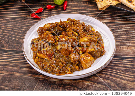 Bowl of traditional spicy chicken curma with flatbread, chilies, and exotic vegetables on a rustic dark wood table. Bowl of traditional spicy chicken curma with flatbread, chilies, and exotic vegetables on a rustic dark wood table. 138294049