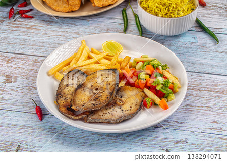 Fried fish steaks with french fries, lemon, and side dishes on a rustic blue wooden table Fried fish steaks with french fries, lemon, and side dishes on a rustic blue wooden table 138294071